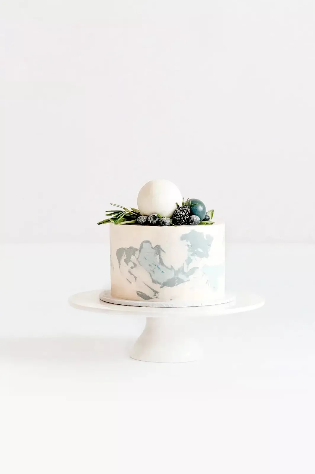 Elegante zweist&ouml;ckige Hochzeitstorte auf wei&szlig;em St&auml;nder mit grauem Vogeldesign und gr&uuml;ner Blattdeko auf der Oberseite.