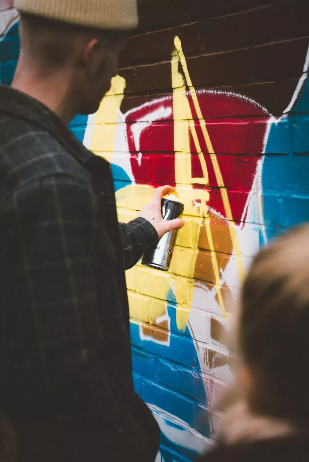 Teilnehmer beim Sprayen einer gro&szlig;en blauen Wand mit gelben und roten Elementen als Teambuilding-Aktivit&auml;t.