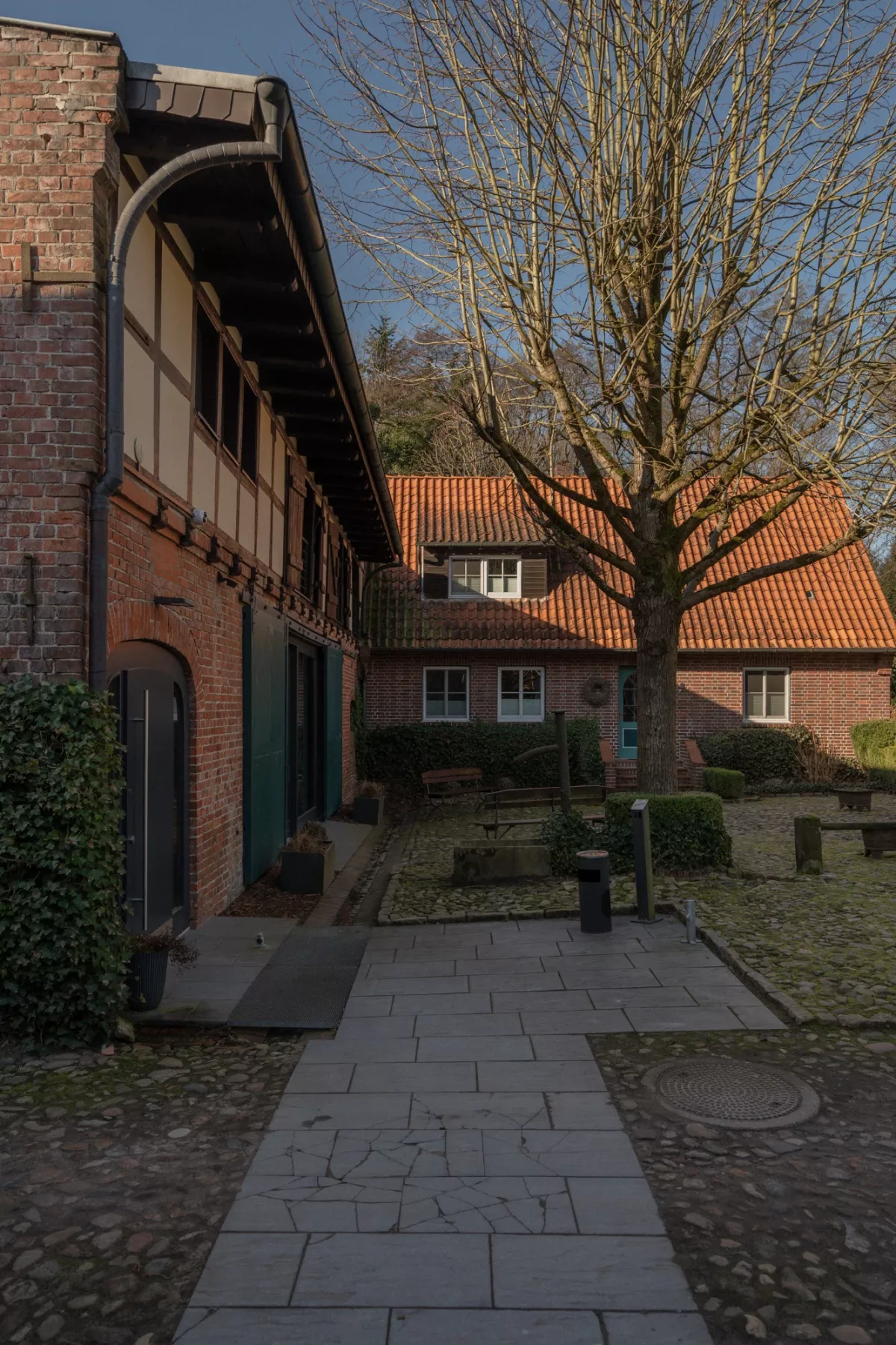 Gepflasterter Innenhof mit Backsteingeb&auml;uden, orangeroten Dachziegeln und kahlem Baum an einem sonnigen Wintertag.