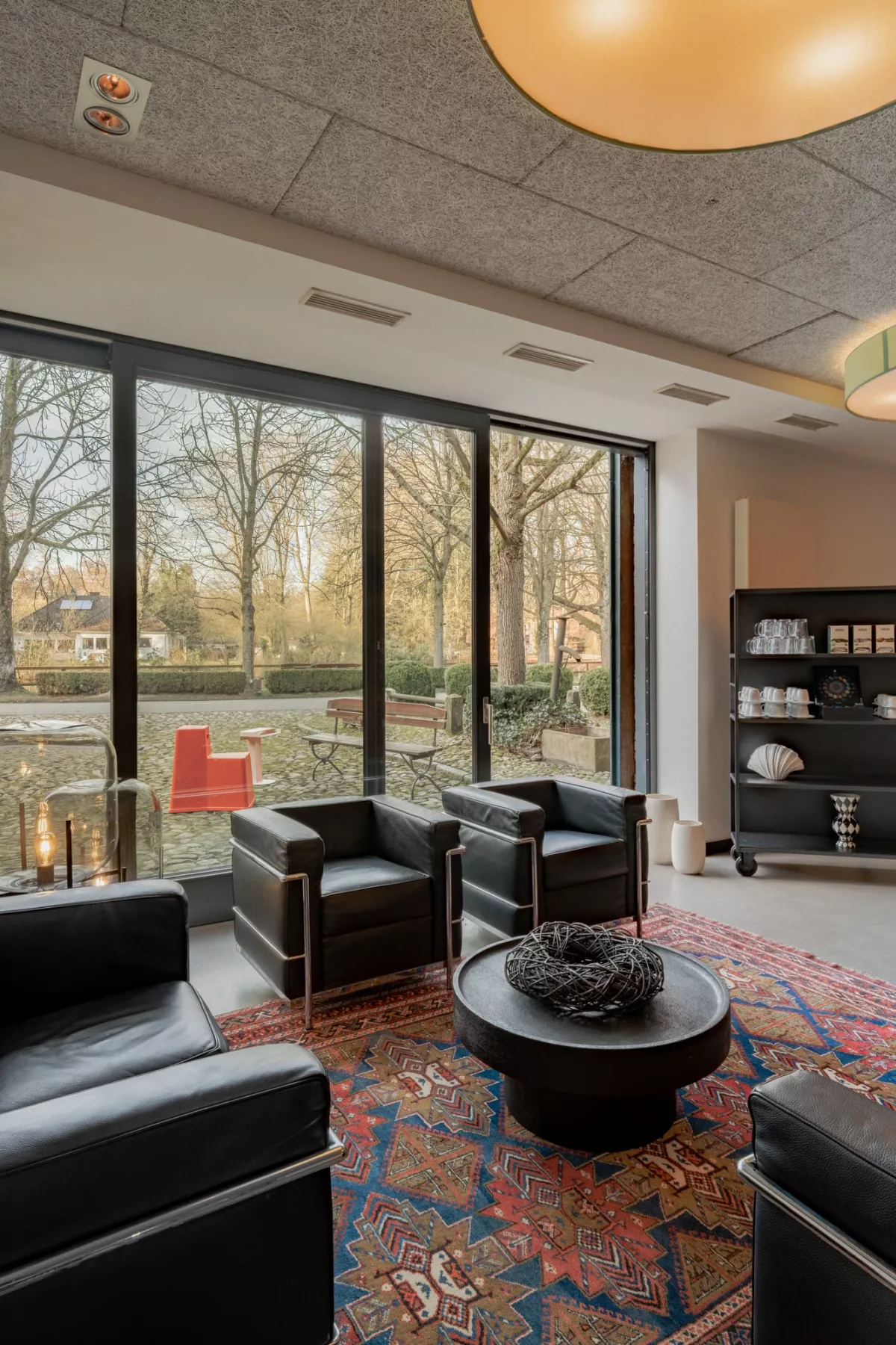 Modernes Foyer mit schwarzen Lederm&ouml;beln, rundem Couchtisch und gro&szlig;er Fensterfront zum Park, Kamin und B&uuml;cherregal im Hintergrund.