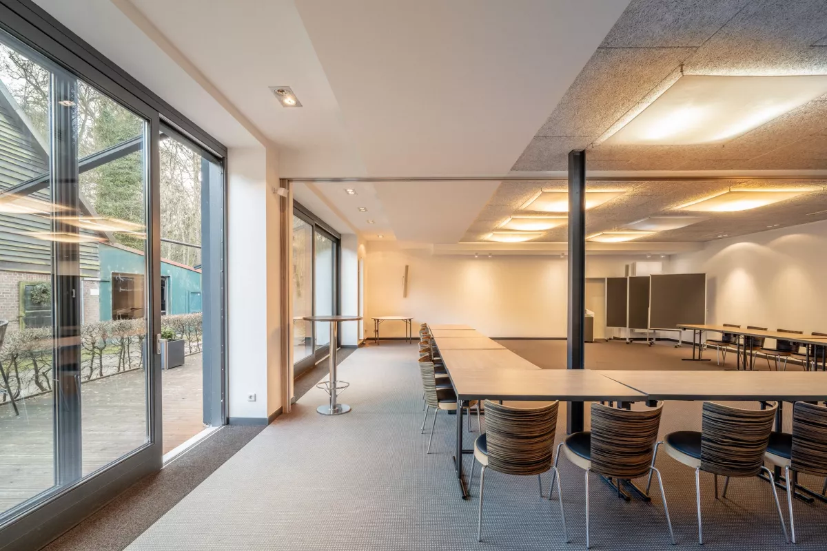 Moderner Konferenzraum mit gro&szlig;en Glasfenstern, Holztischen und ergonomischen St&uuml;hlen, nat&uuml;rliches Licht und helles Raumdesign.