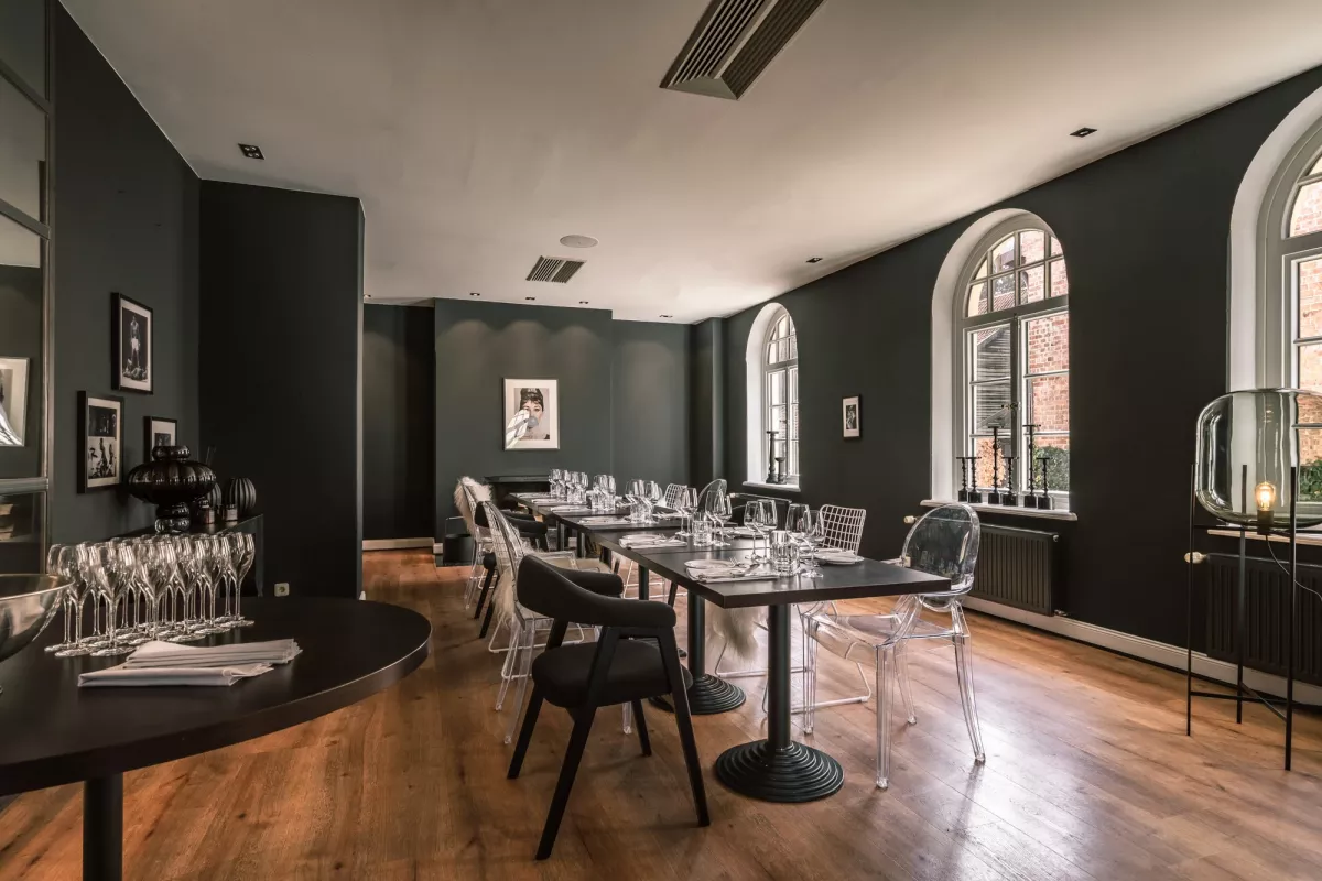 Eleganter Veranstaltungsraum mit dunkelgr&uuml;nen W&auml;nden, Holzboden, gedecktem Tisch und modernen St&uuml;hlen, gro&szlig;e Fenster mit Blick nach au&szlig;en.