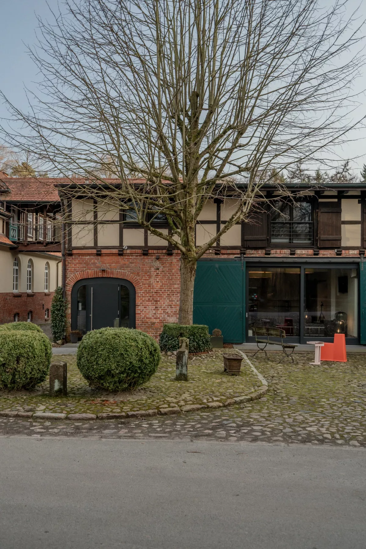 Historisches Fachwerkgeb&auml;ude mit Backsteinfl&uuml;gel, kahlem Baum und runden Buchsb&auml;umen.