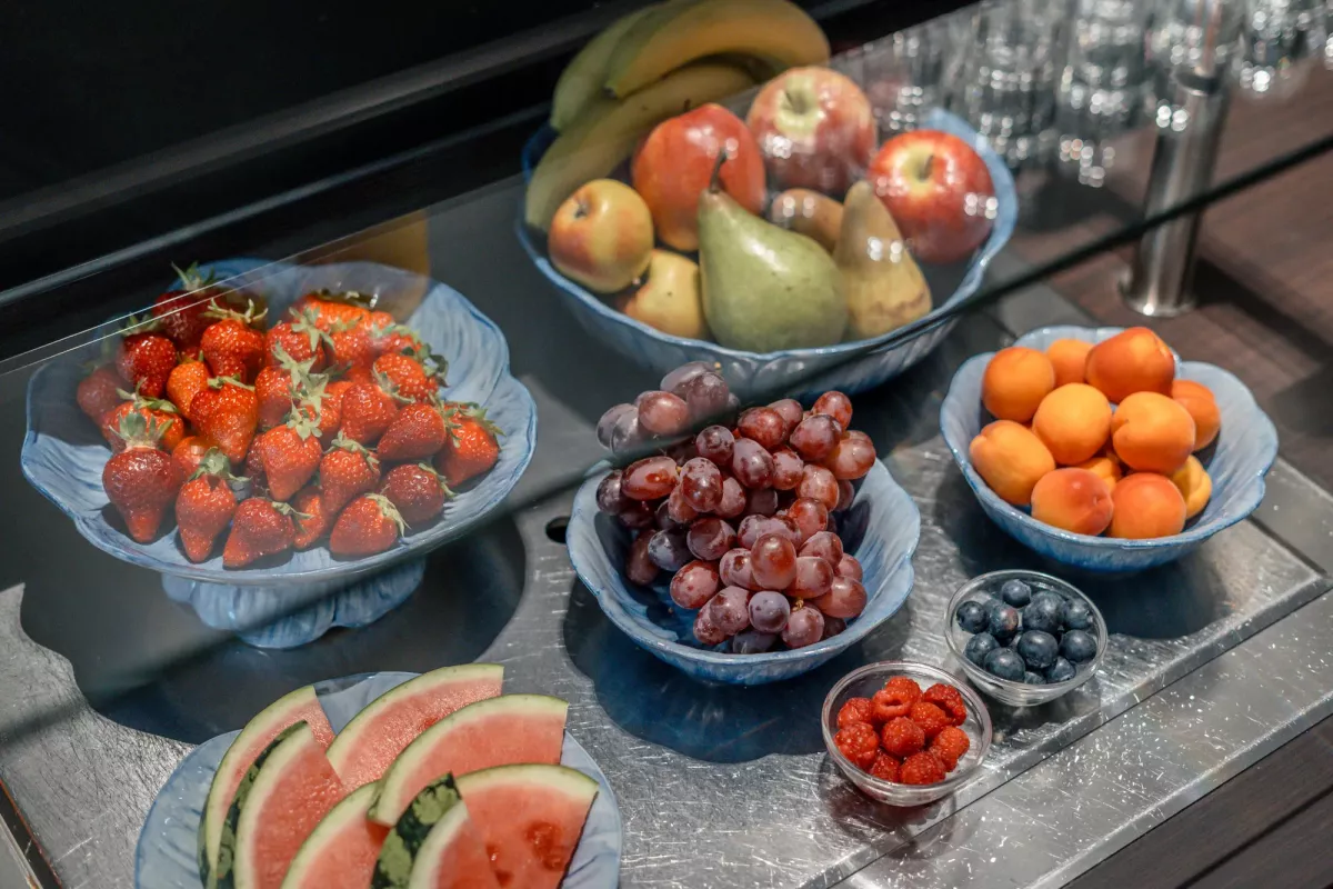 Frische Fr&uuml;chte auf Serviertellern: Erdbeeren, Trauben, Aprikosen, Melone und diverses Obst in Schalen arrangiert.