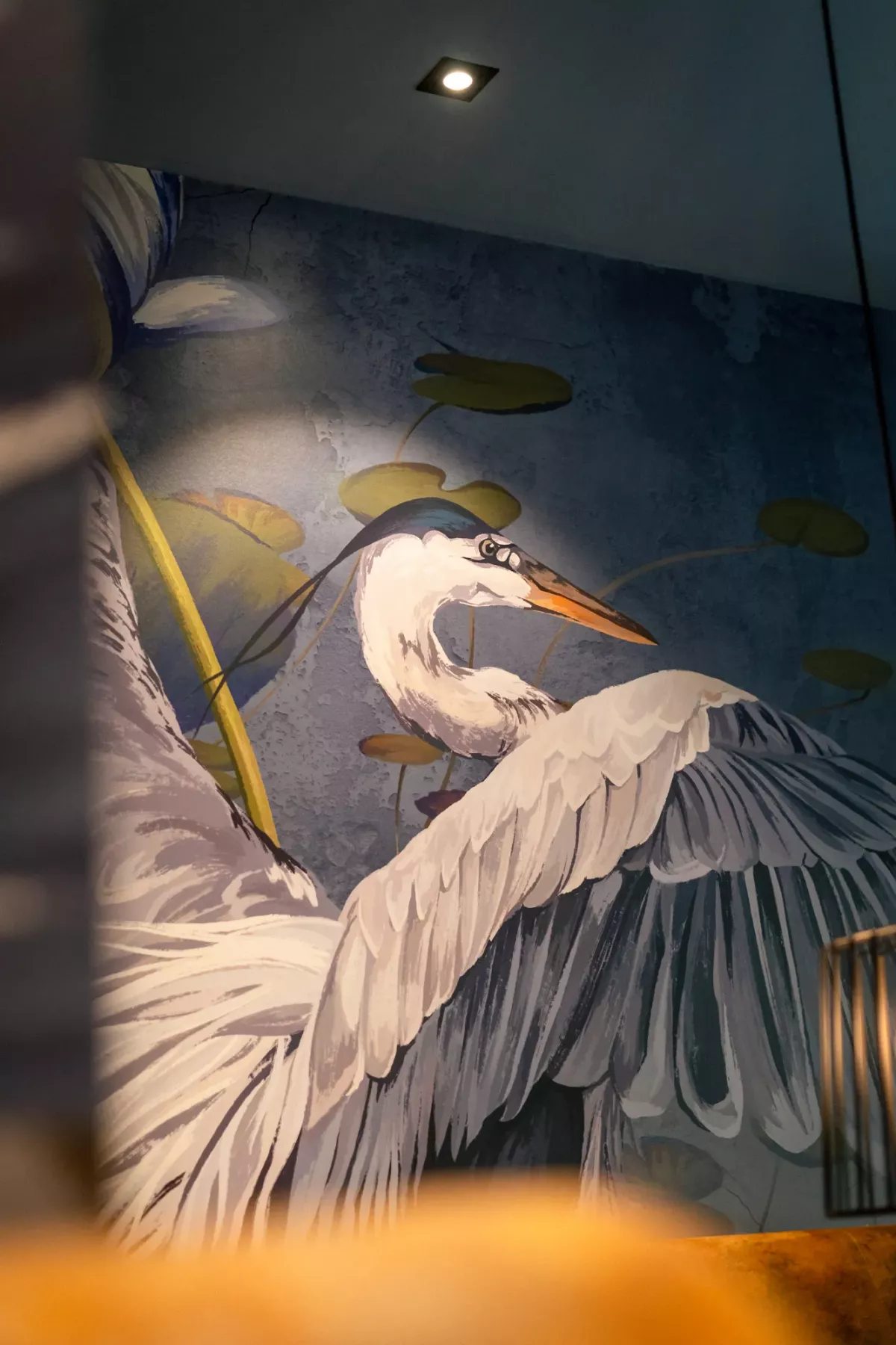 Gro&szlig;er Reiher mit ausgebreiteten Fl&uuml;geln an der Wand gemalt, umgeben von Wasserlilien, in eleganter Inneneinrichtung.