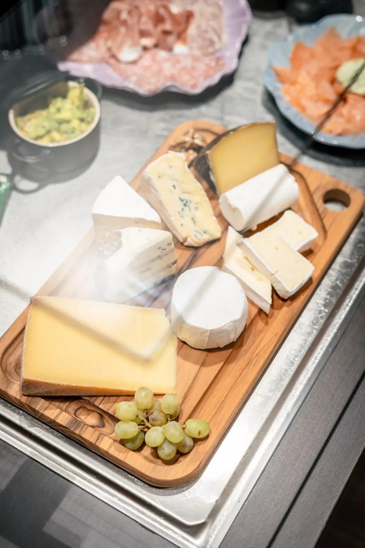 K&auml;seplatte auf Holzbrett mit verschiedenen K&auml;sesorten und Trauben, arrangiert als Fr&uuml;hst&uuml;cksbuffet